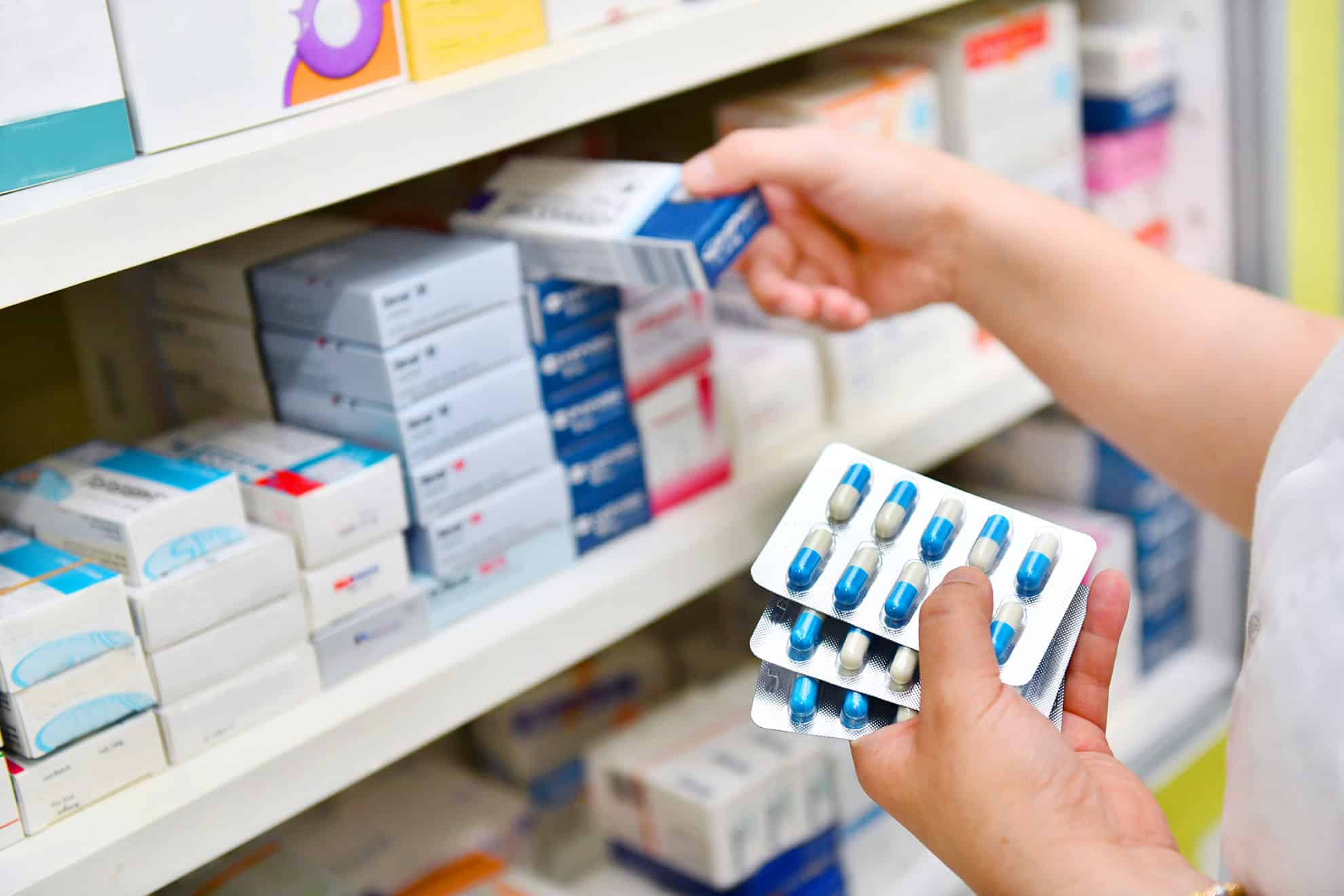 Pharmacist holding medicine box and capsule pack in pharmacy drugstore.