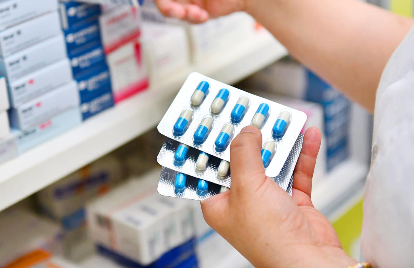 Pharmacist holding medicine box and capsule pack in pharmacy drugstore.