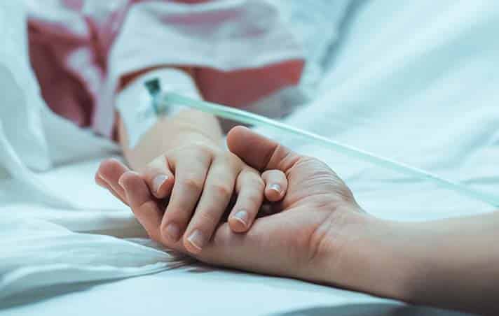 Young patient holding hand with a parent in hospital
