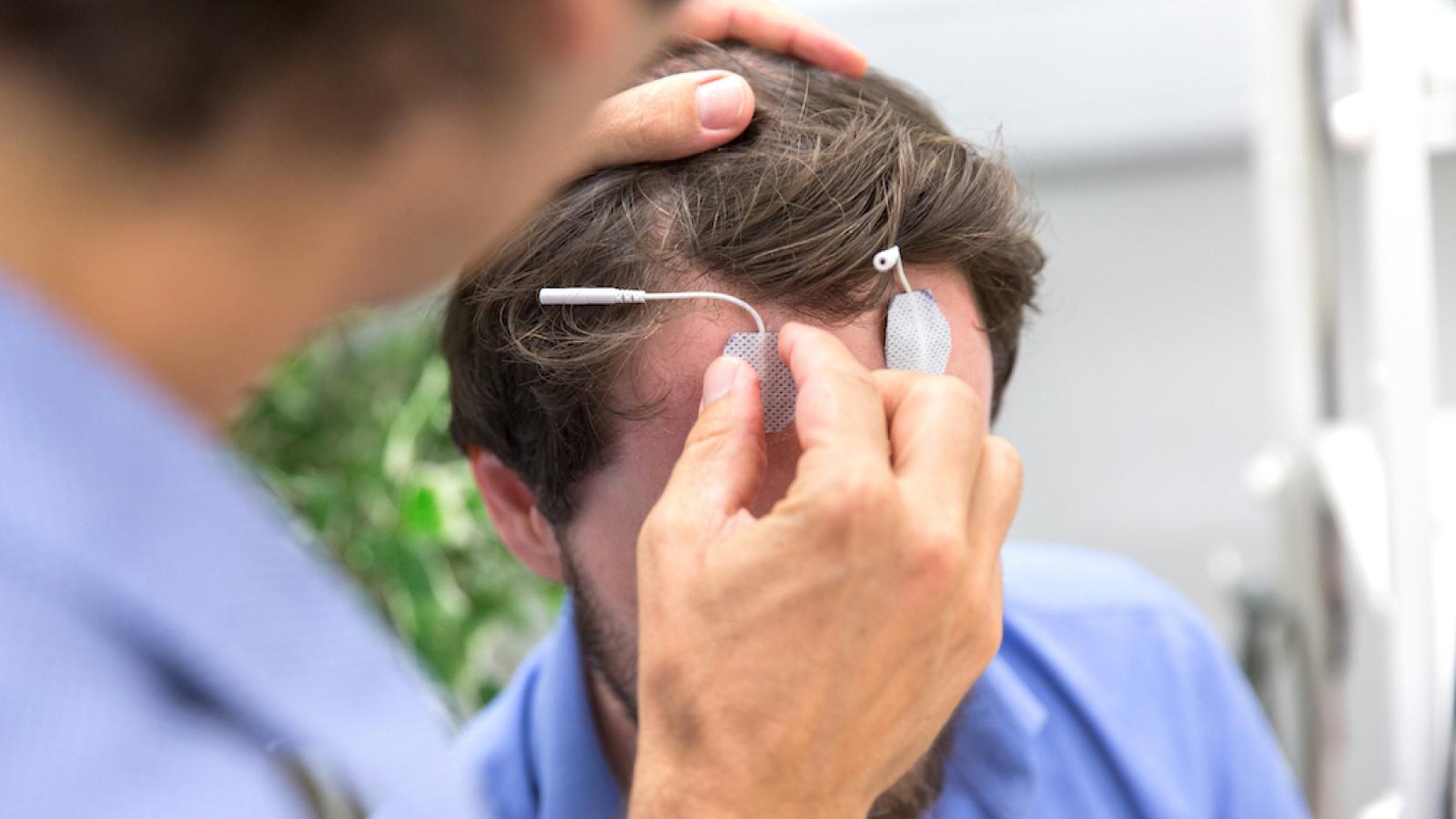 Healthcare professional placing electrodes on male's forehead to measure brain stimulation.