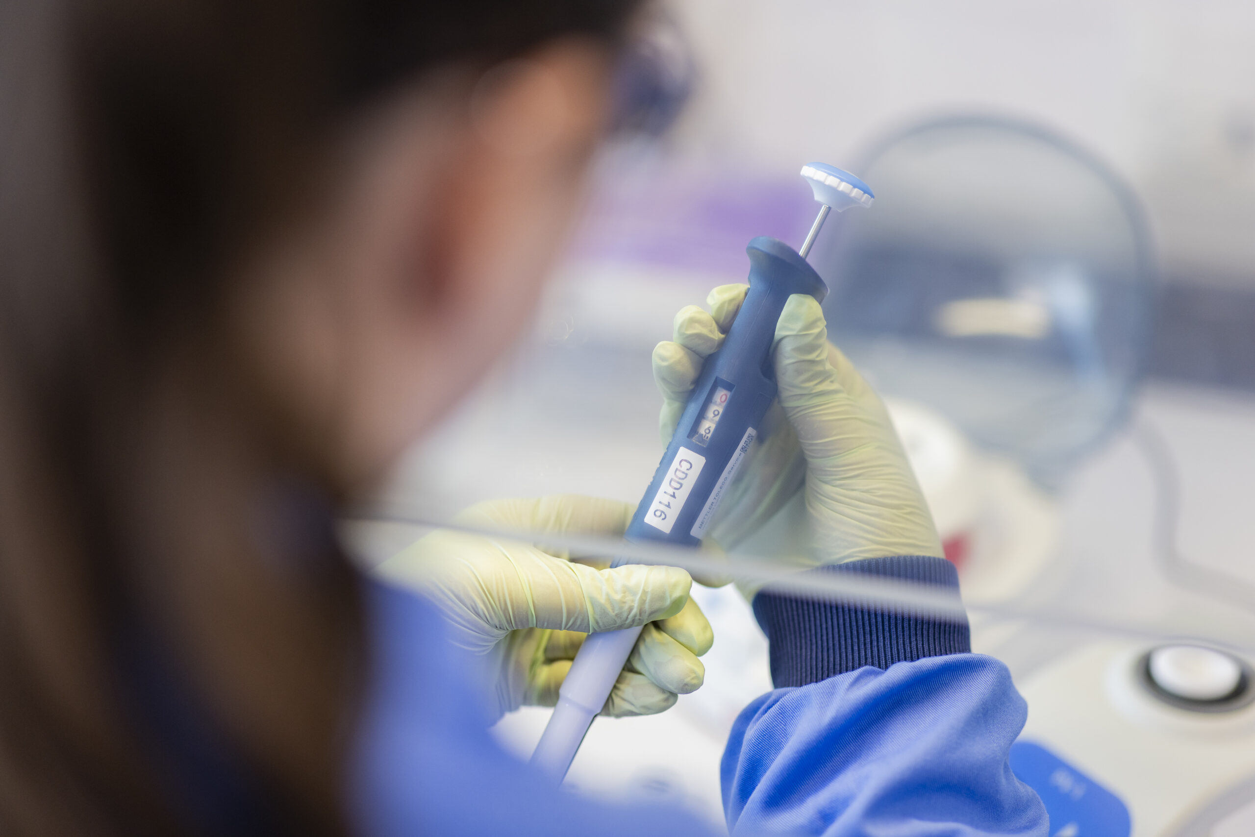 A female scientist wearing PPE is holding a pippette and looking at it
