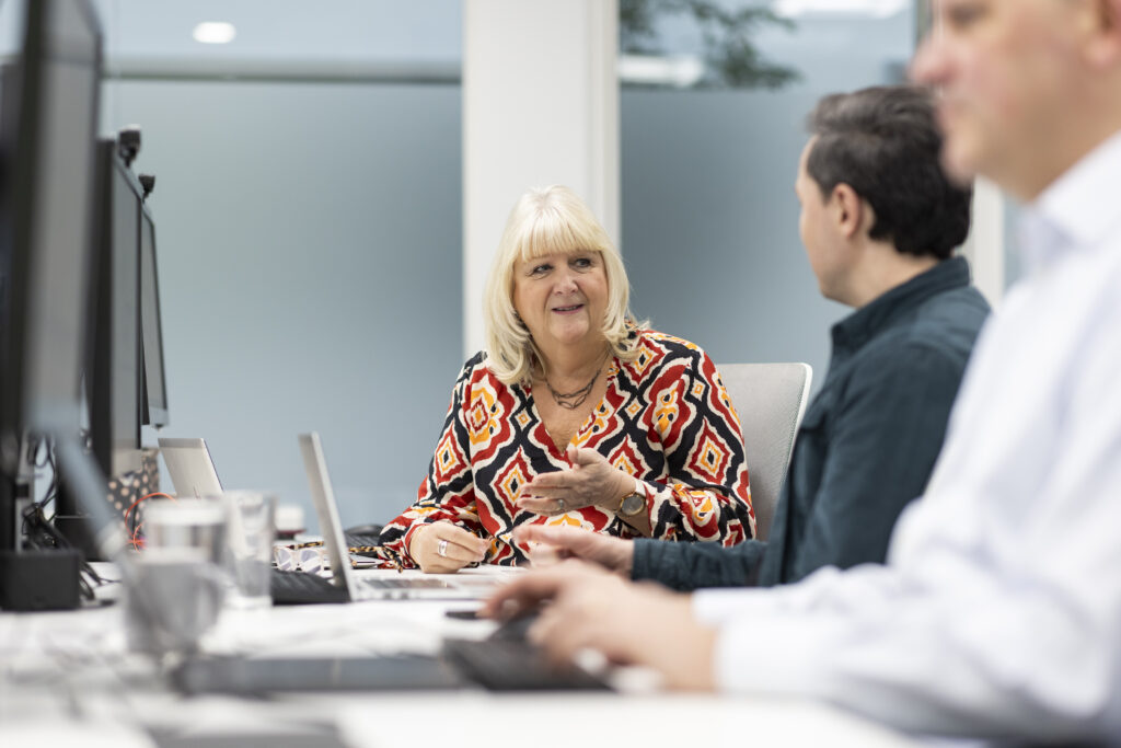 Three LifeArc colleagues sit at their desks, two of them in discussion.