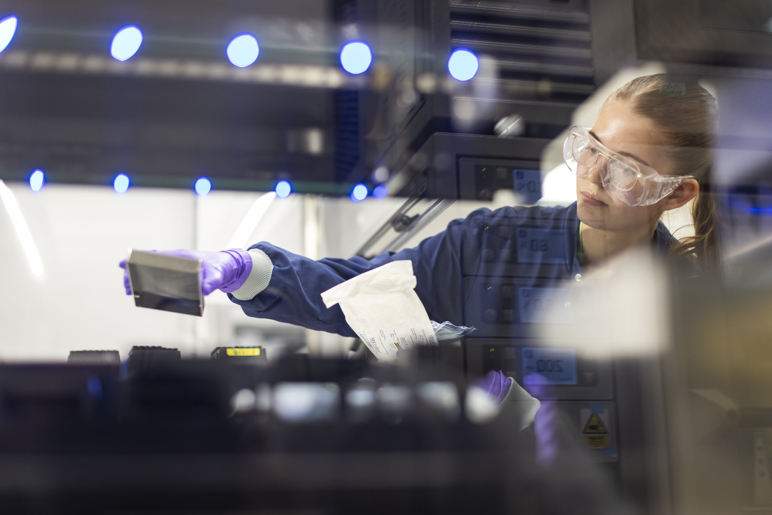 A female scientist wearing PPE is in the lab carrying out an experiment
