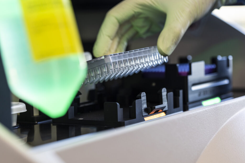 Image of a scientists gloved hand removing samples from a piece of lab equipment