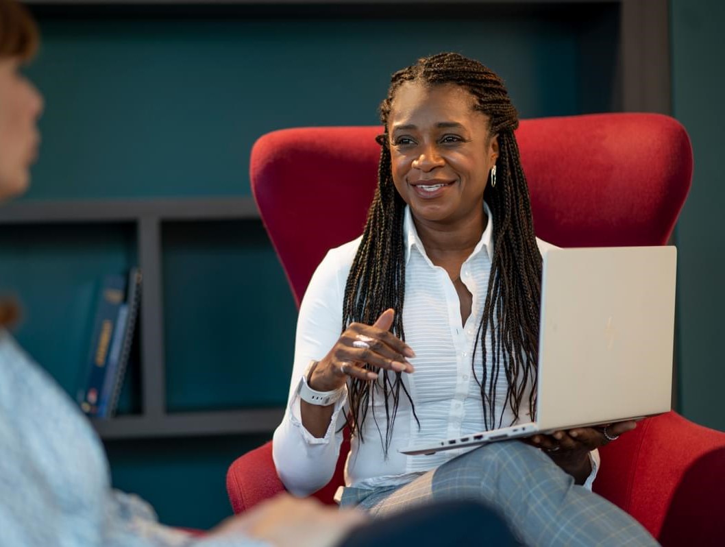 LifeArc colleague Anji sits in an armchair smiling at a colleague just out of shot, her laptop on her knee