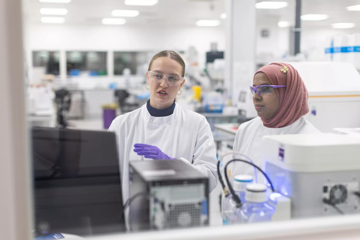 Two female LifeArc scientists stand at a lab bench looking at a computer screen.