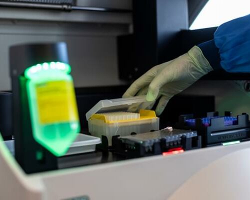 A gloved hand reaches into a piece of lab equipment to check samples in vials
