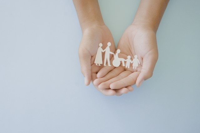 Two hands cradle a string of paper dolls including children and adults, one is a wheelchair user.