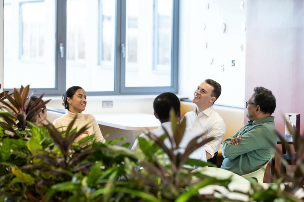 A group of LifeArc colleagues sit around a table having a conversation in a communal office space