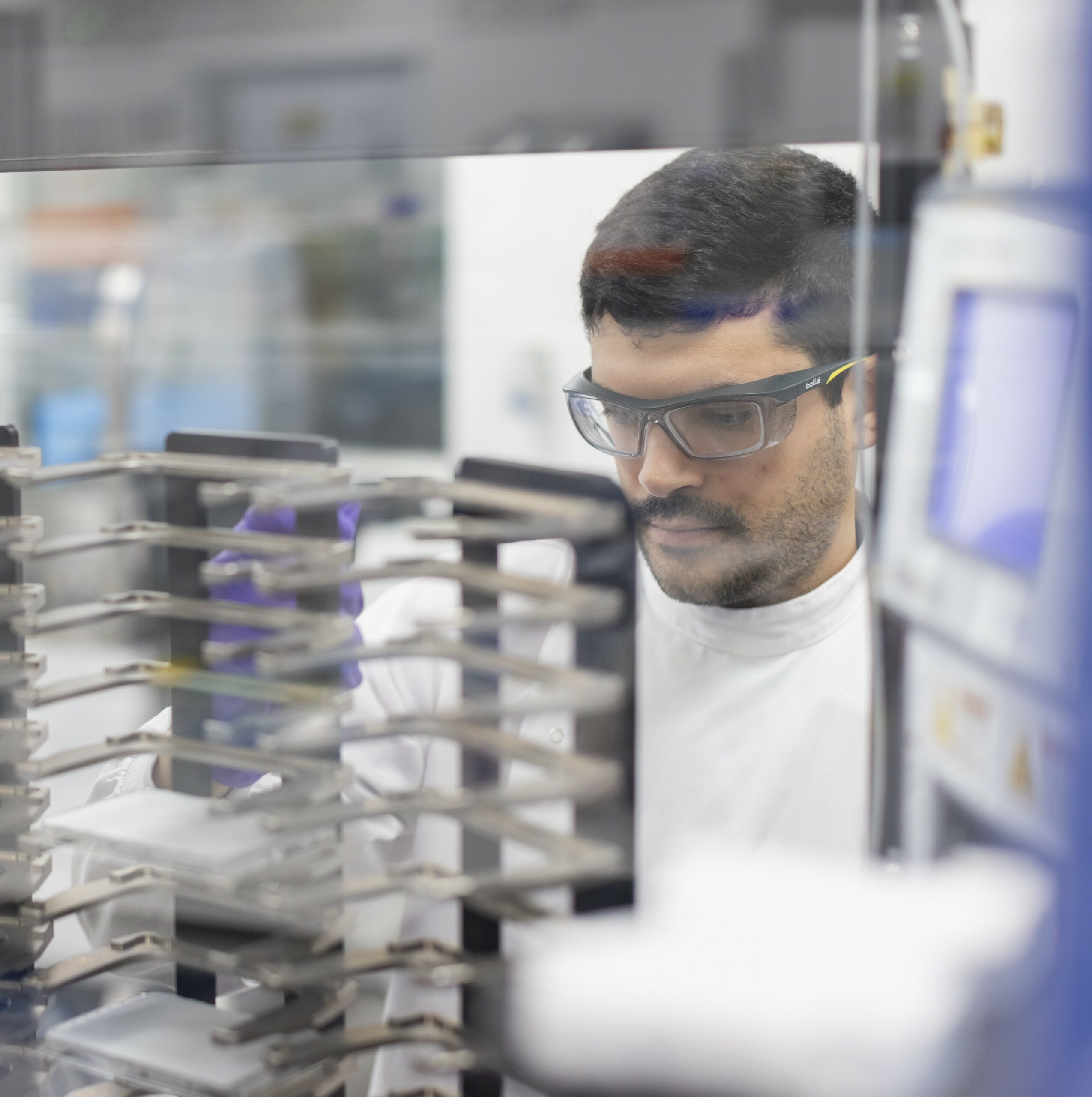 LifeArc scientist Joao Pisco stands operating lab equipment, wearing a lab coat, gloves and safety glasses.