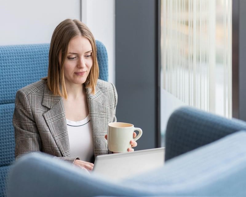 A LifeArc colleague sits in a large chair by a window, typing on her laptop, a mug in her hand