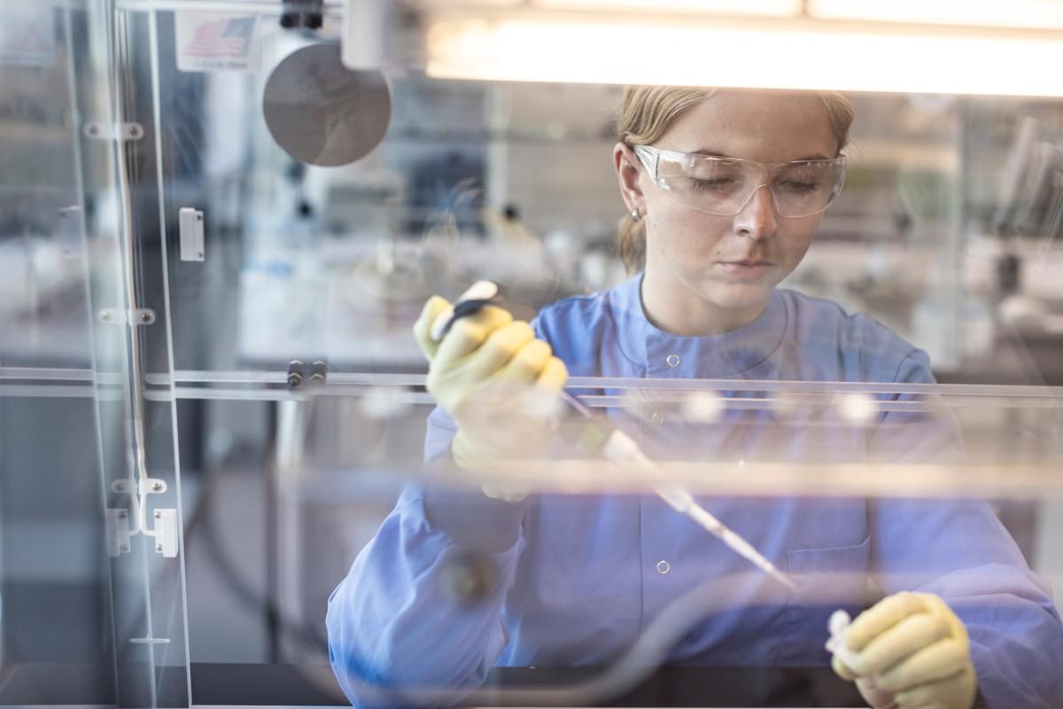 Female LifeArc Scientist pipettes liquid into a vial under a fume hood.