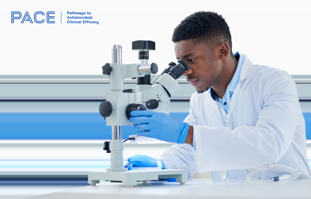 A black male scientist wearing PPE is looking through a microscope