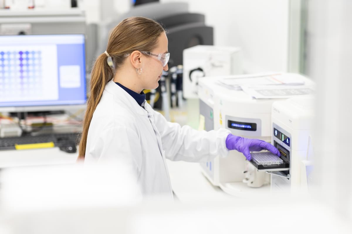 A female LifeArc scientist loads a plate into a lab machine
