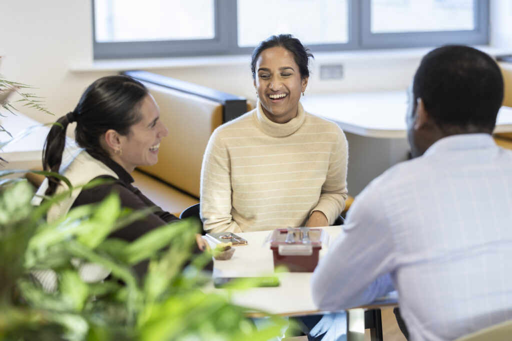 Three people laughing around the table in the LifeArc office
