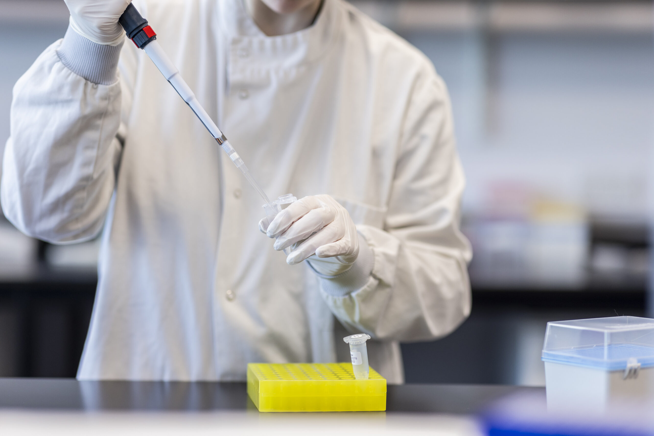 A scientist in a white lab coat pipettes liquid into a small vial.