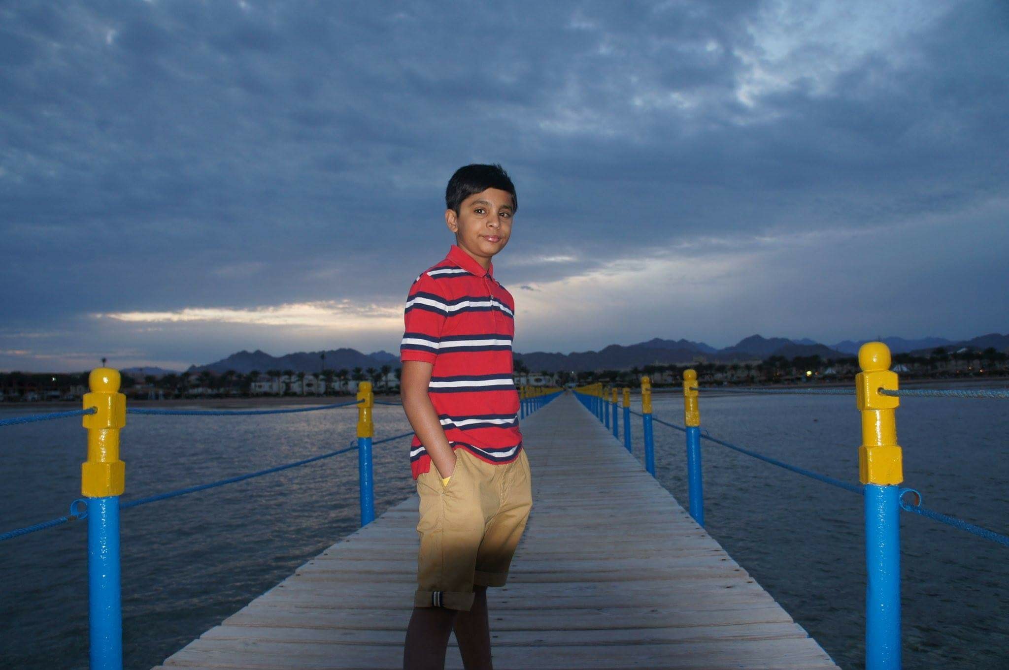 A portrait of Khushil on a bridge leading across a large estuary