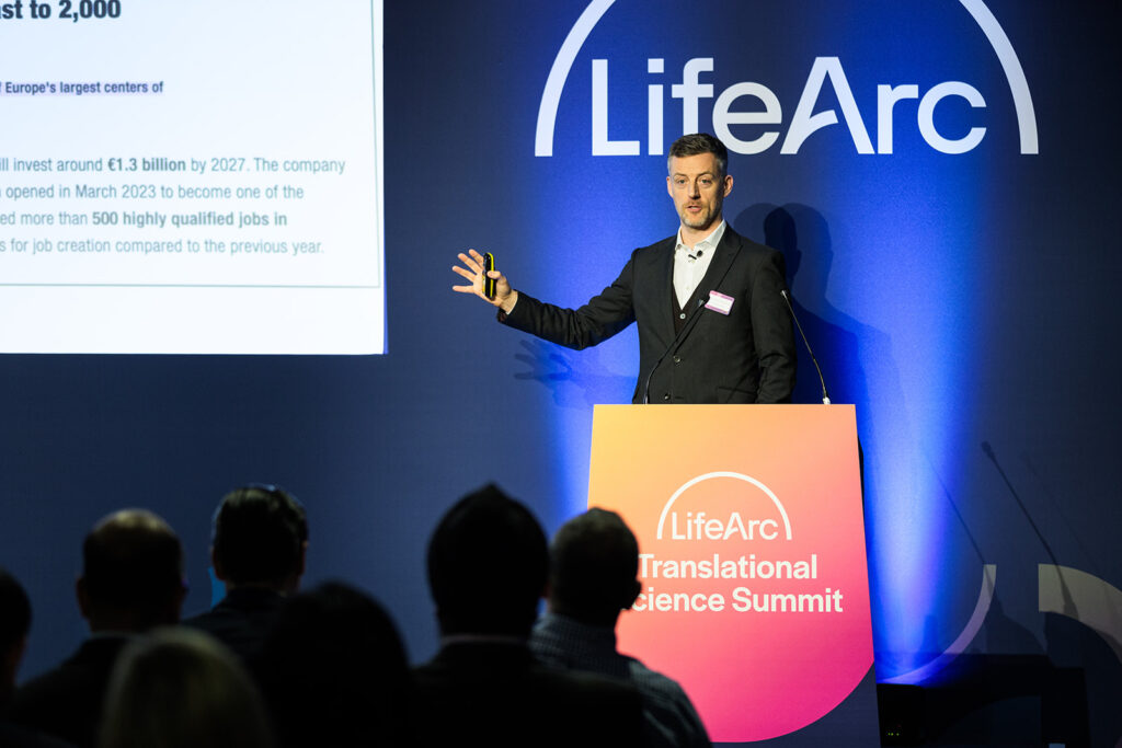 Lord James O'Shaughnessy giving a presentation at a lectern at the LifeArc Translational Science Summit.