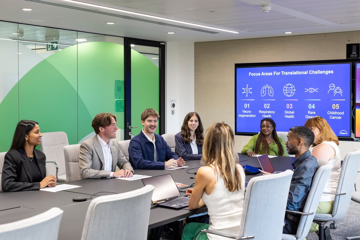 Group of LifeArc fellows sat in a meeting room around a table talking