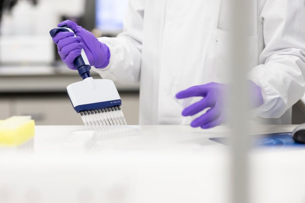 Close up of the hands of a scientist wearing gloves pipetting