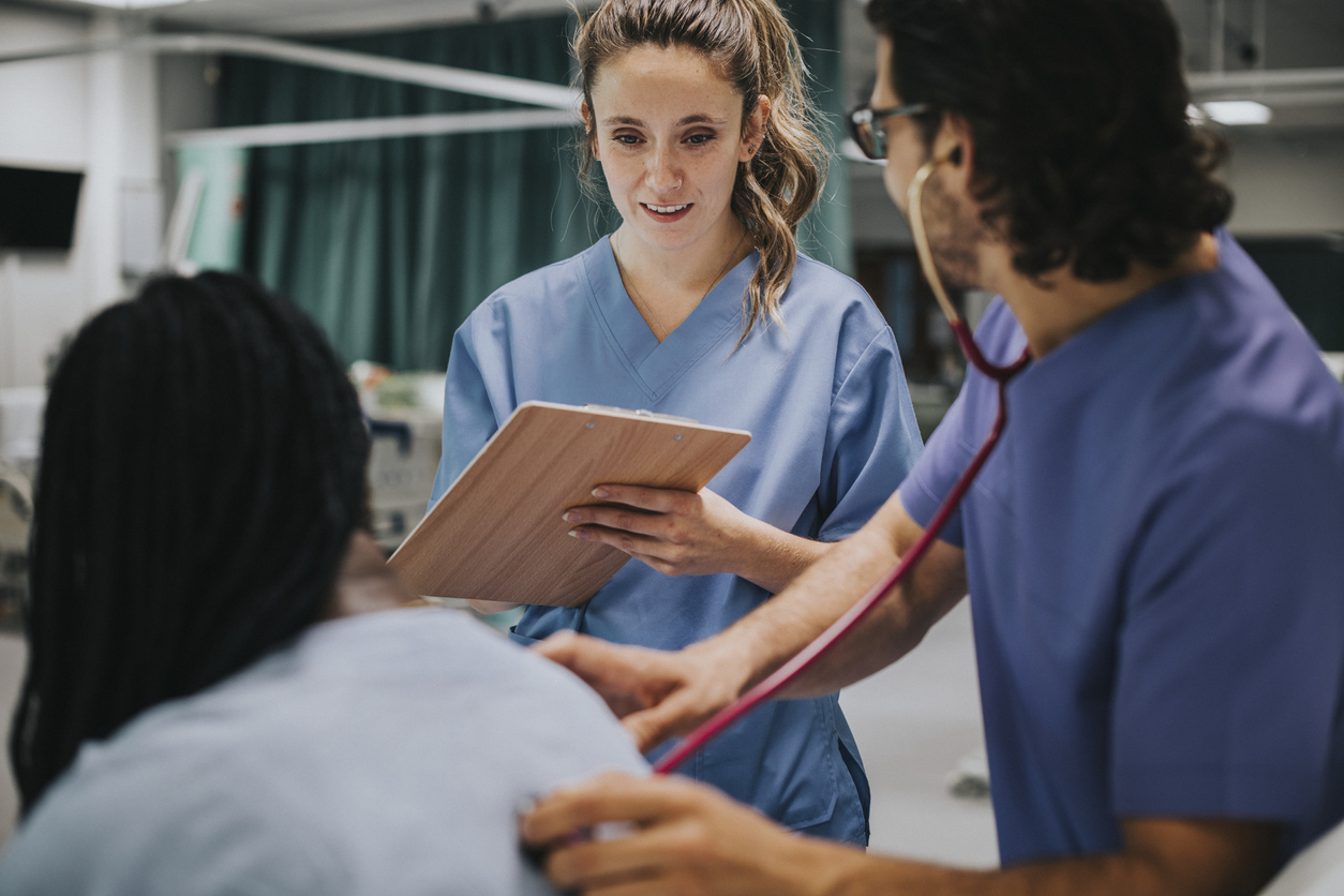 Young male physician examining a patient and female physician is taking notes