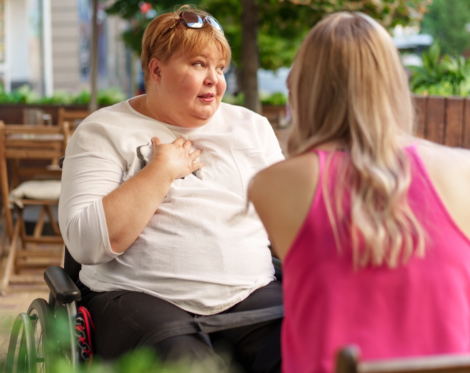 Mother with disability in wheelchair talking to her daughter while sitting at the table in cafe in the street