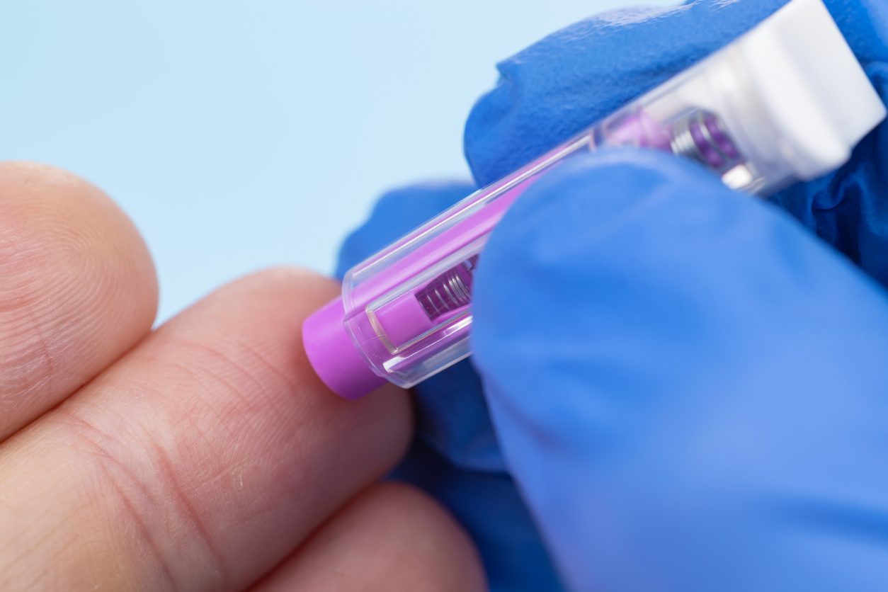 Doctor piercing patients finger with automatic lancet in clinic. Taking blood for close-up analysis, a clinical blood test. Finger prick.