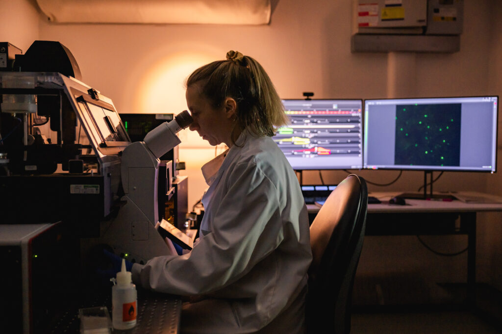 Female scientist at The LifeArc Centre for Rare Respiratory Diseases looking through a microscope 