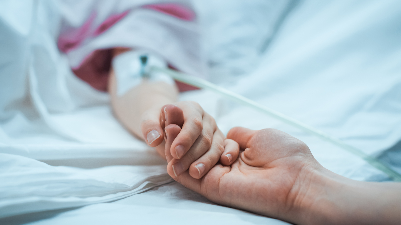Recovering child lying in a hospital bed sleeping with mother holding hand