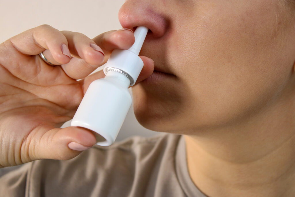 Close up of a woman using a nose spray against a white background